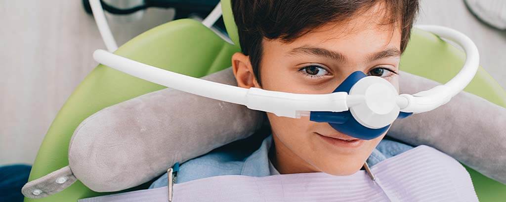 a young boy thinks about sedation dentistry as his dentist puts on a mask